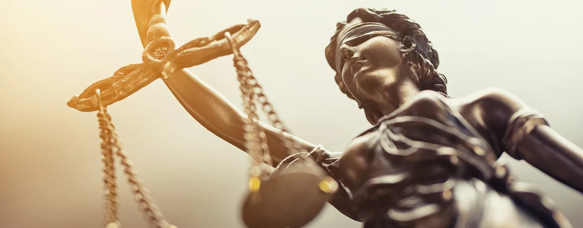 A close-up, low-angle shot of a bronze statue of Lady Justice with scales and a blindfold